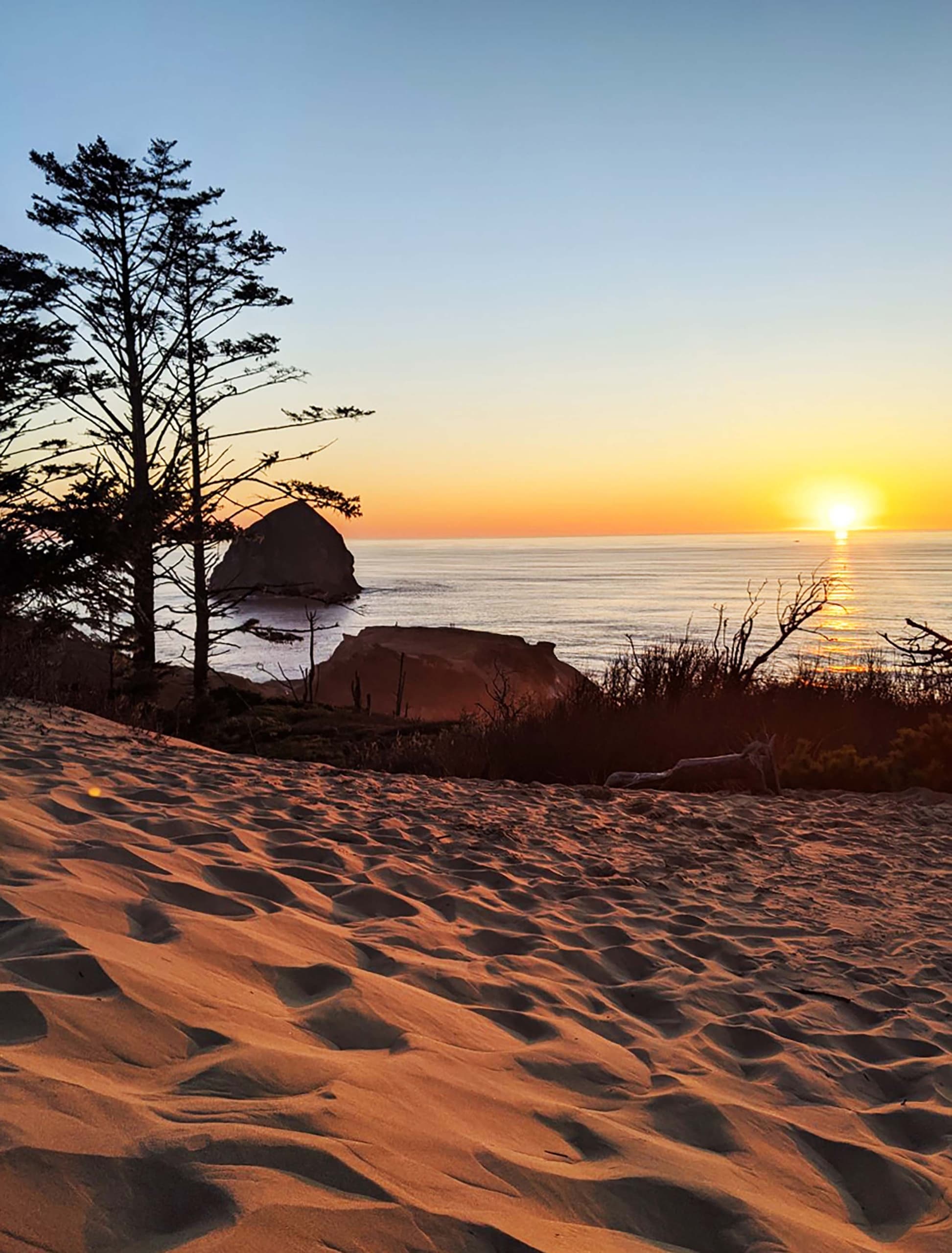 A Cape Kiwanda dune hike at sunset with the sun shining on the sand as it disappears