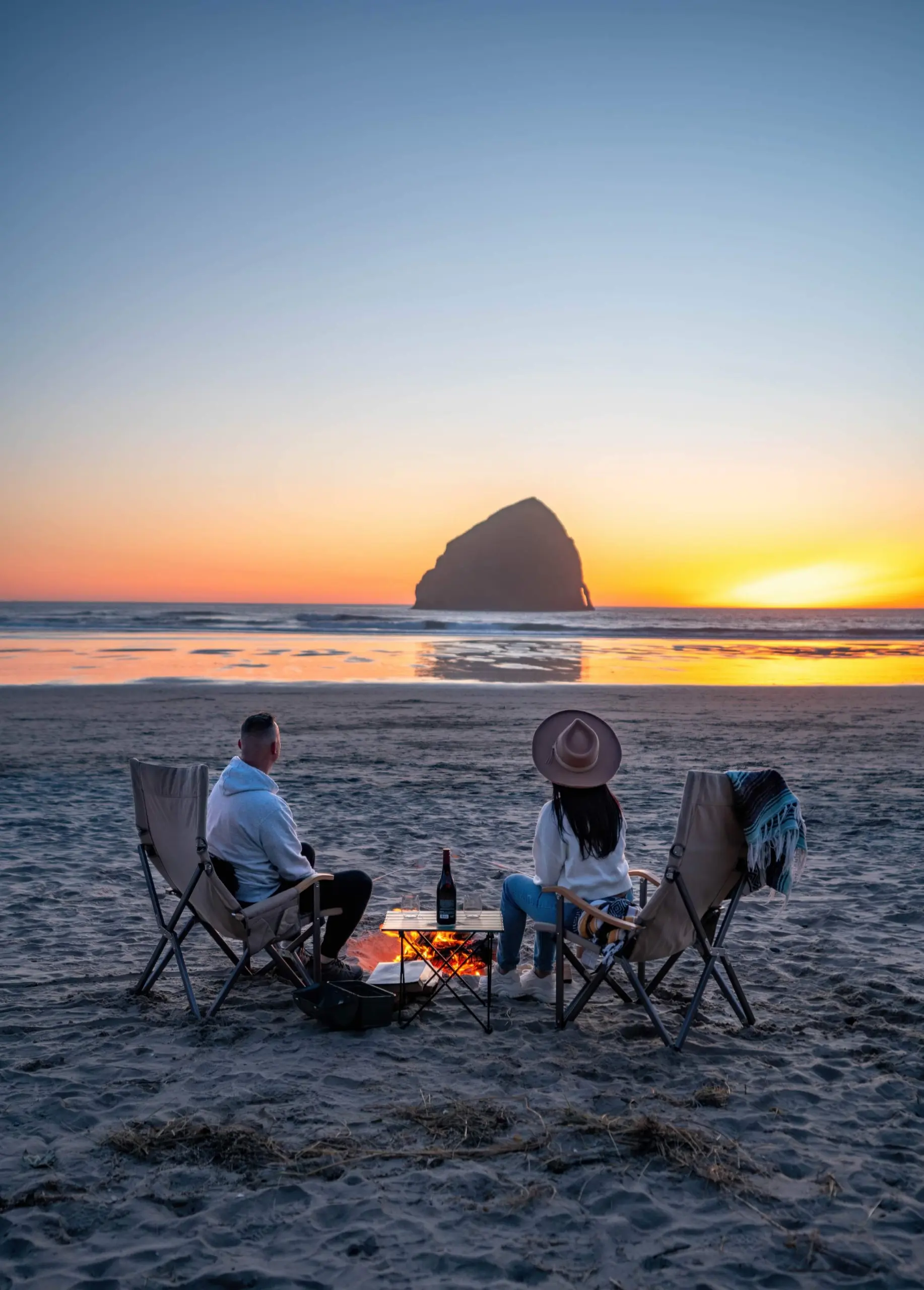 A couple watching the sunset around the haystack rock with a bottle of wine near headlands