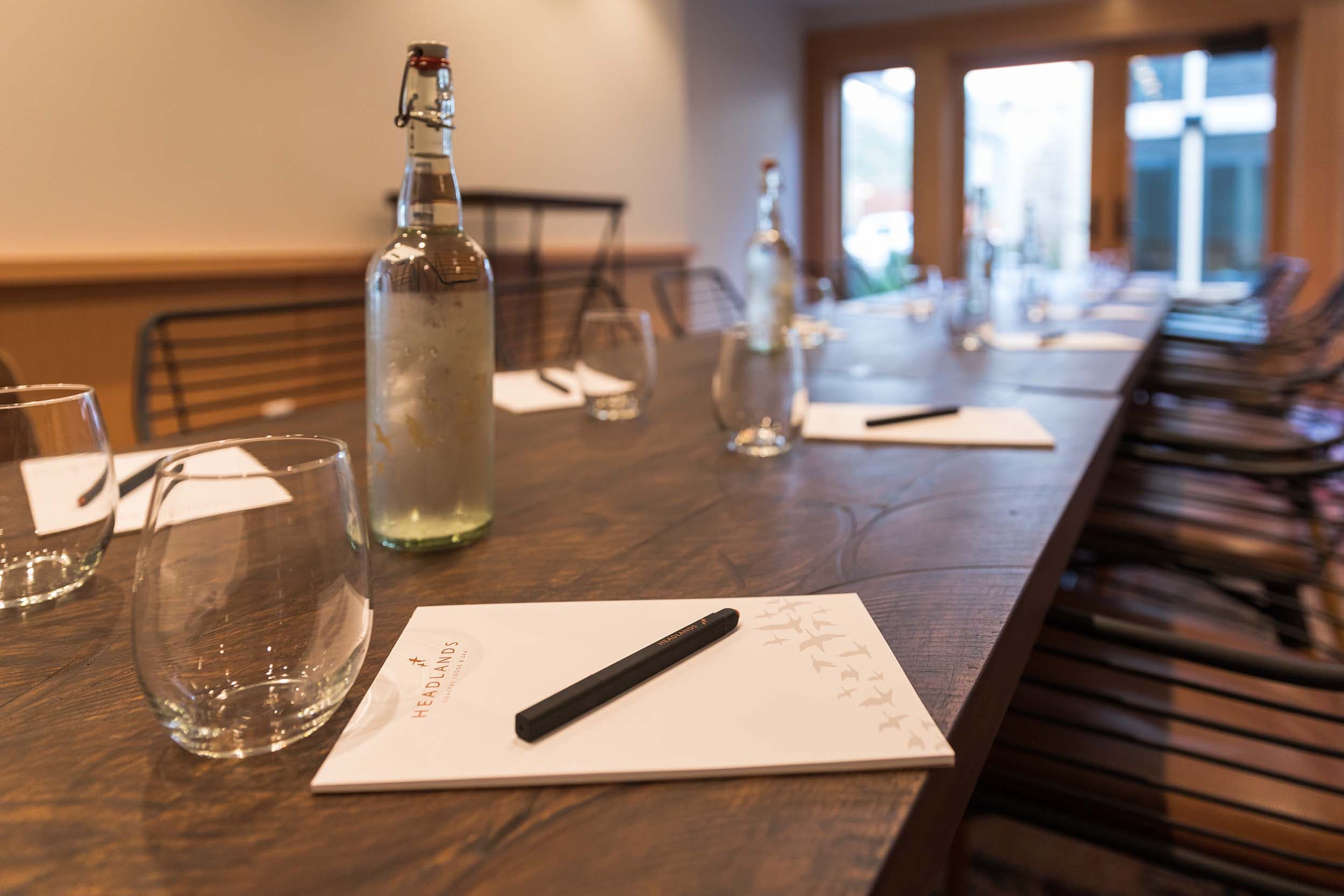 A close up of a pad of paper, pen, water glasses, and water bottles on a table at Longitude