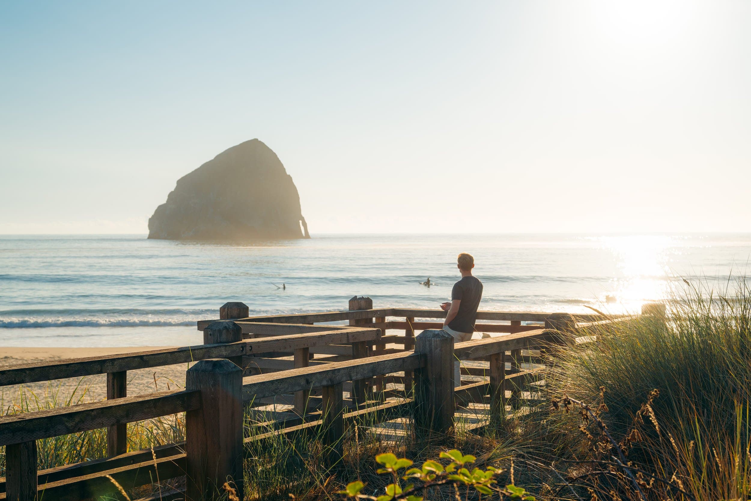 2 surfers in the ocean and a man sitting on the railing of Headlands pathway