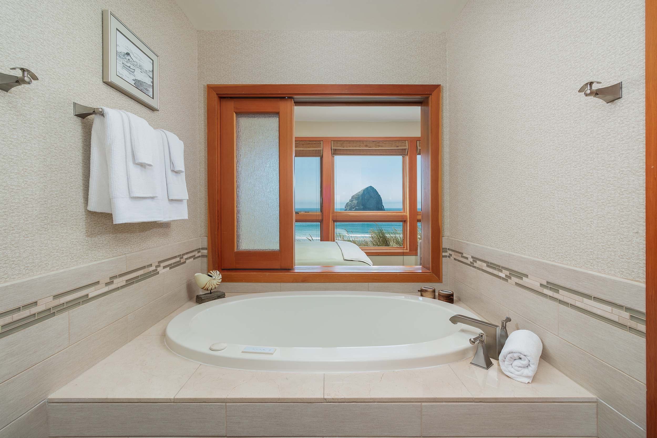 A soaker tub with a view of the ocean and haystack rock in a 3 bedroom cottage at Headlands