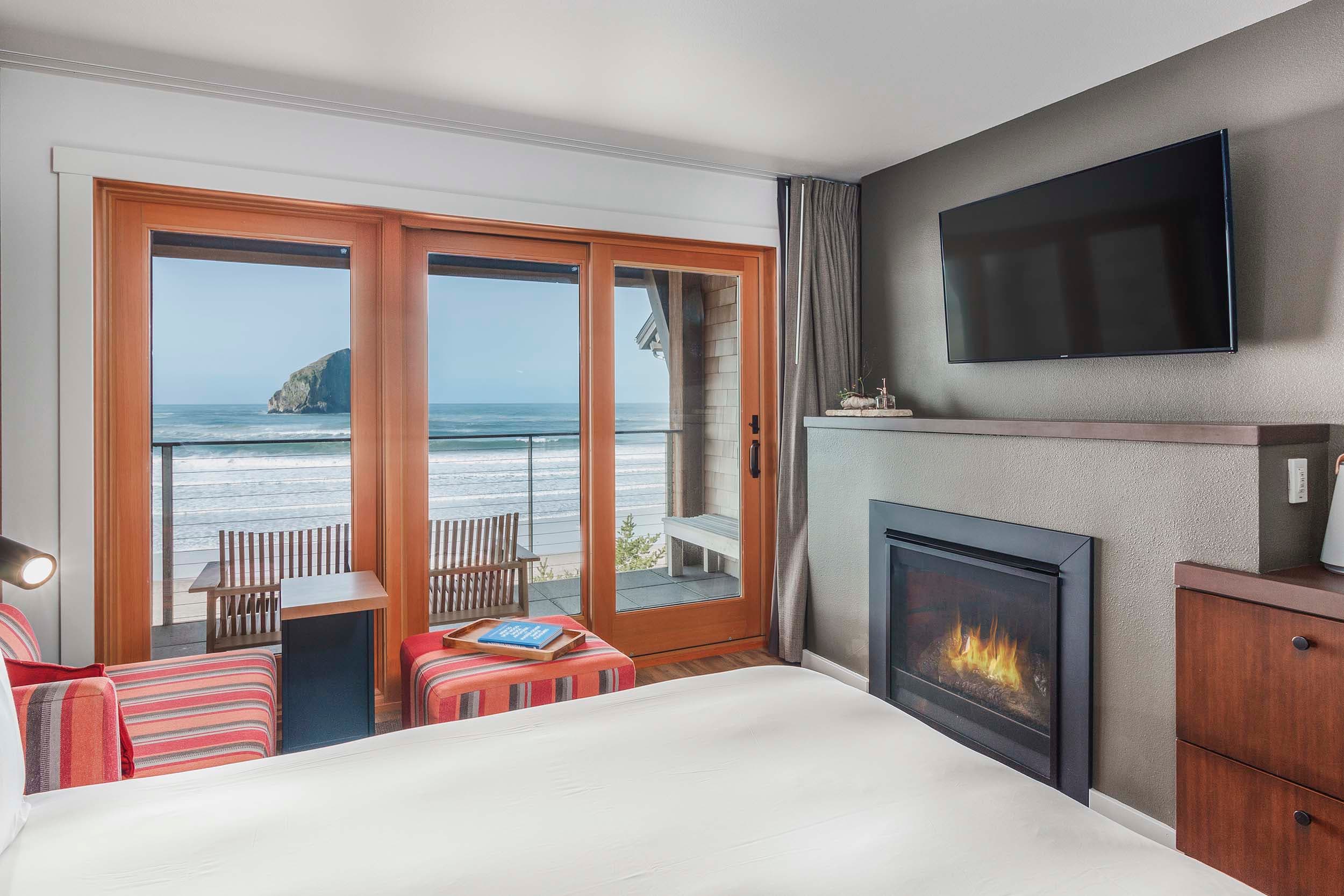 A bed, lounge area with a TV and fireplace, and view of the ocean in a Two Queens Signature room at Headlands