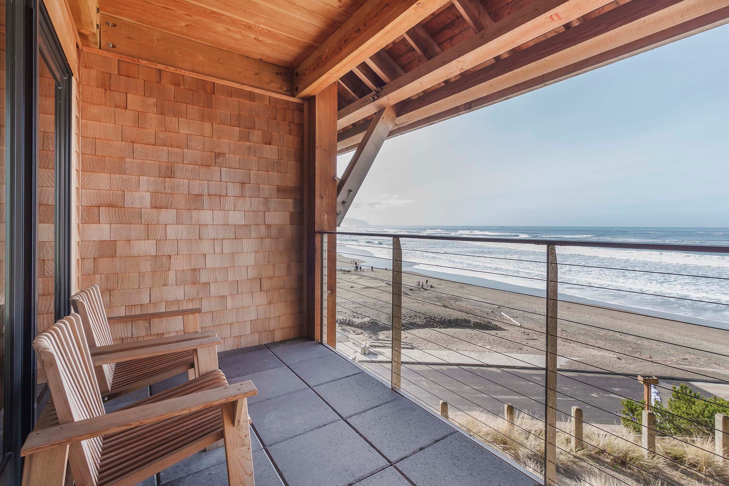 A balcony with 2 wooden lounge chairs facing the ocean in a Two Queens Signature room at Headlands