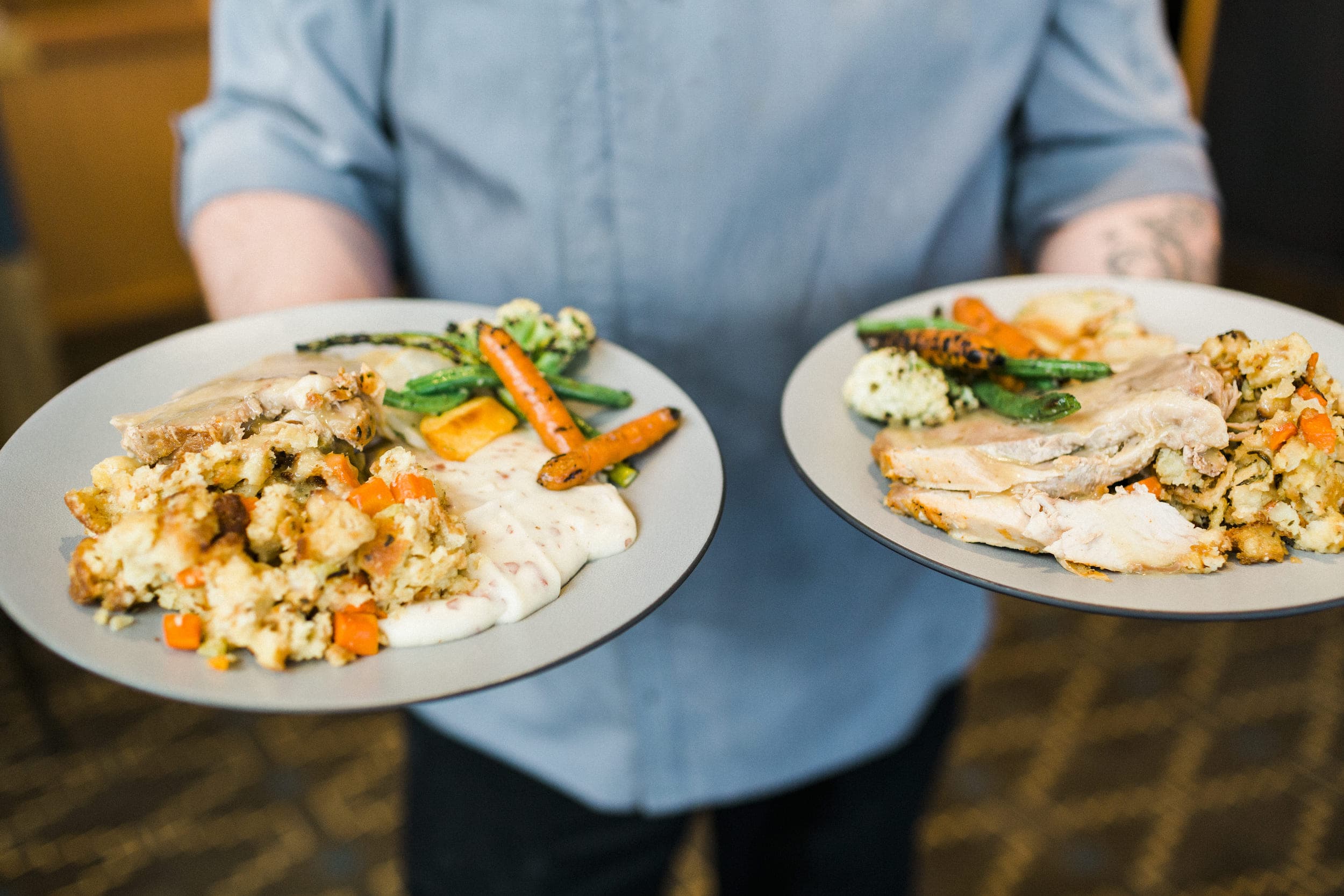 A man holding to plates of Christmas dinner with stuffing, mashed potatoes, carrots, asparagus, and turkey at Meridian Restaurant