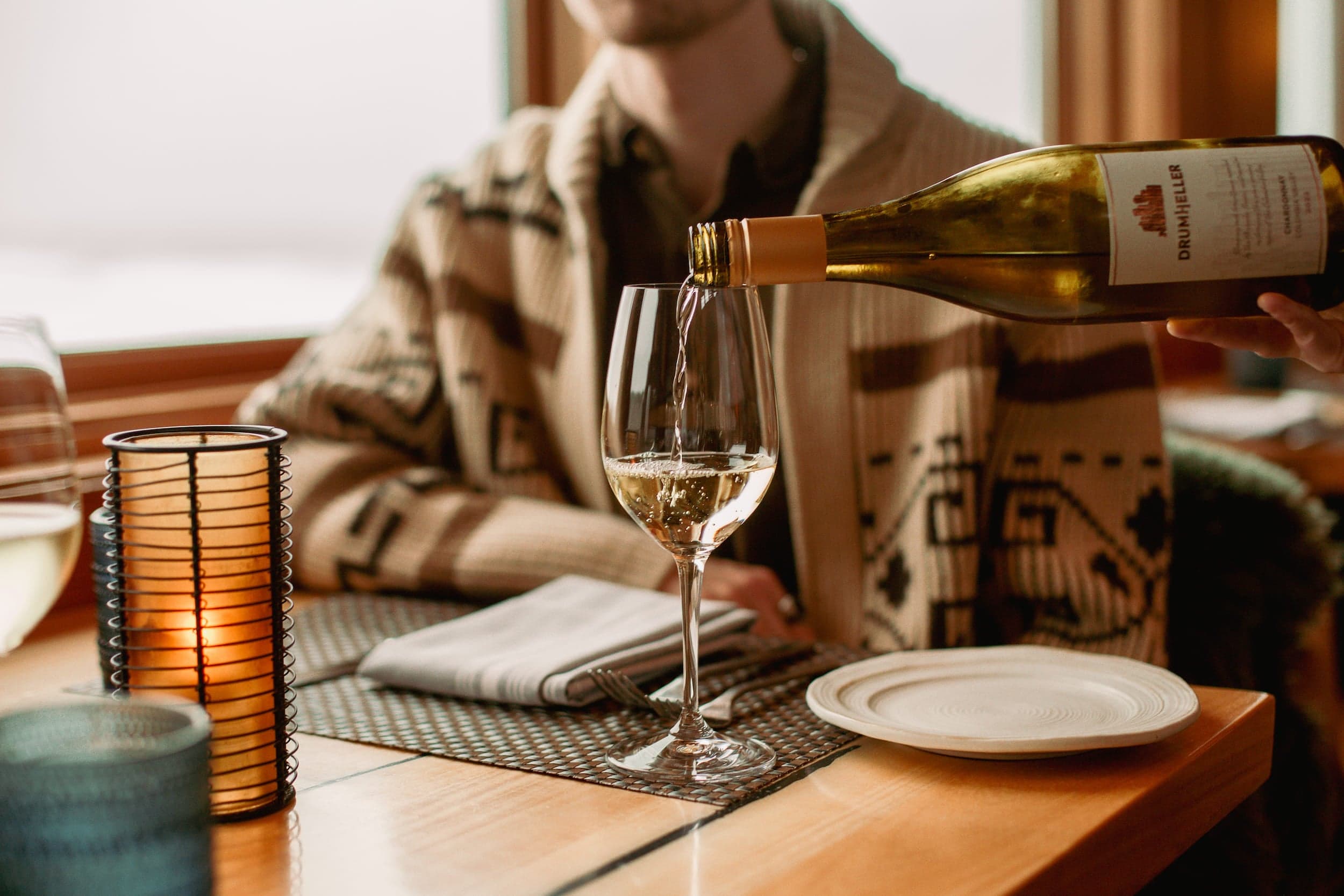 A server pouring a glass of white wine table side for a guest