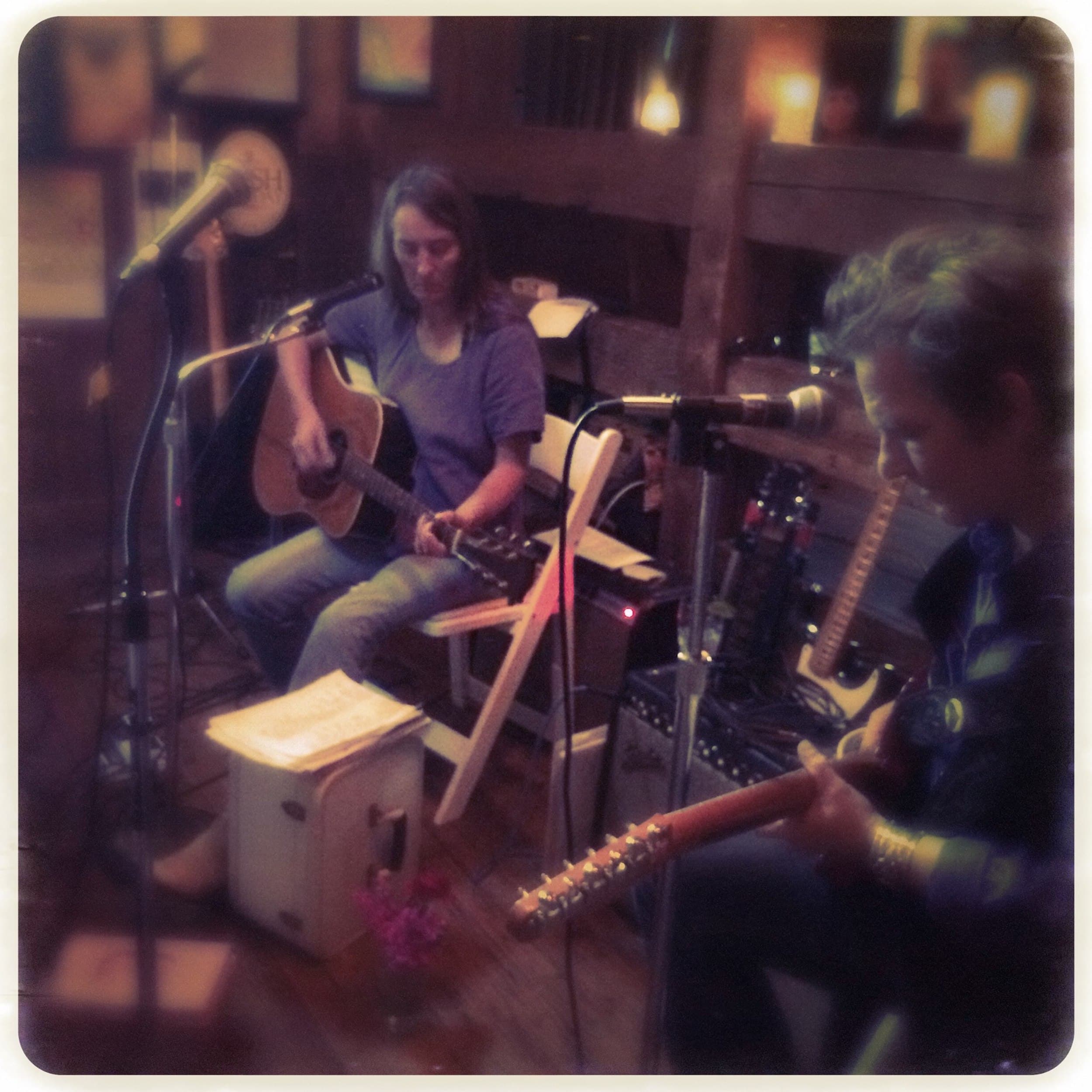 Lynn Conover playing acoustic guitar sitting in a chair on stage at Meridian Restaurant & Bar