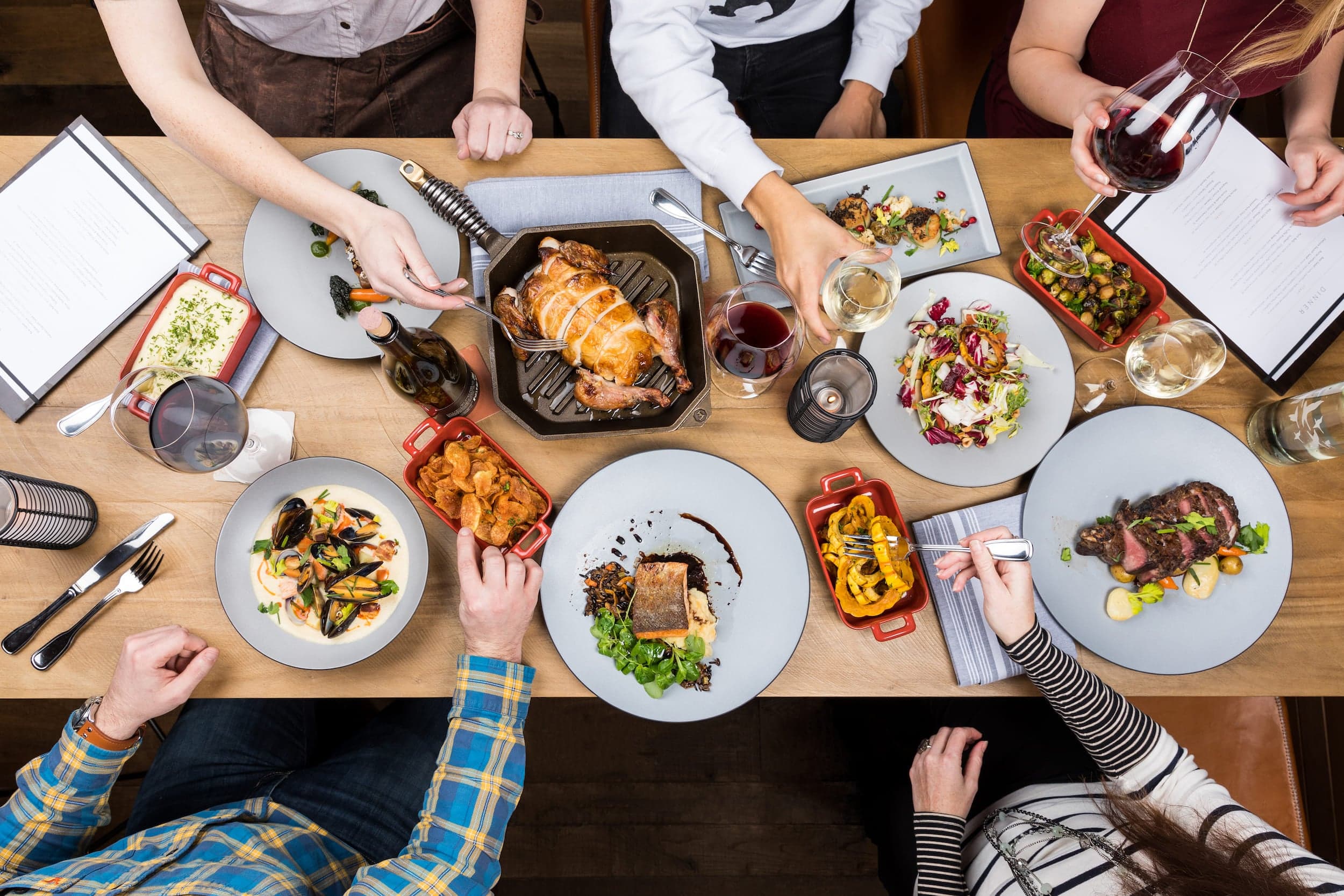 An overhead view of a spread of sharable food at Meridian restaurant such as, steak, chicken, salmon, chowder, and a variety of vegetable dishes